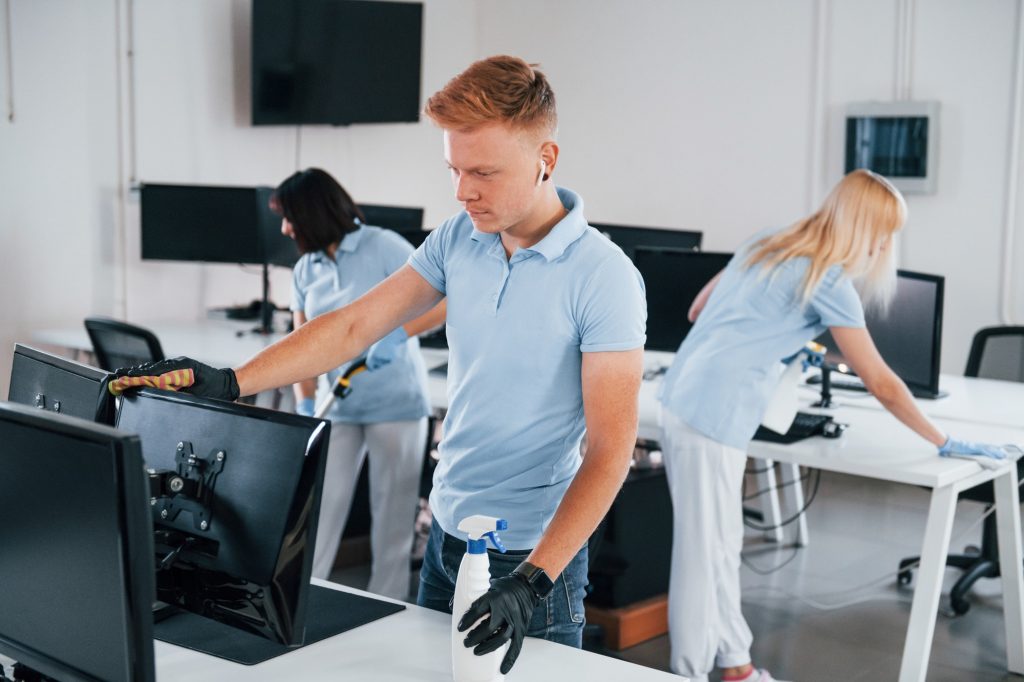 Cleans monitor. Group of workers clean modern office together at daytime